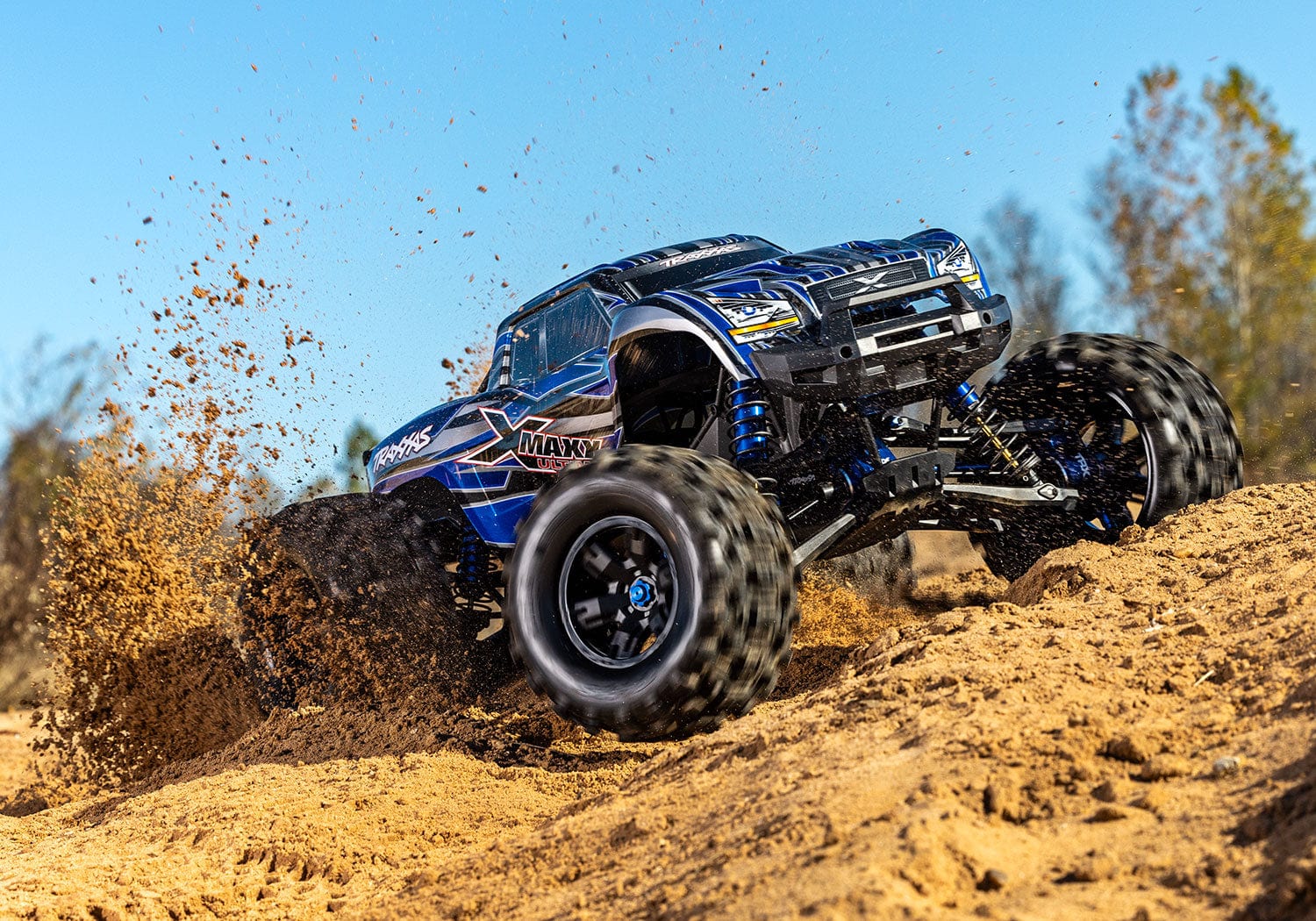 [Action] Traxxas X-Maxx - mavi araç kumlu arazide sürüş halinde