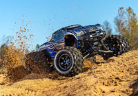 [Action] Traxxas X-Maxx - mavi araç kumlu arazide sürüş halinde