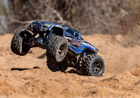 [Action] Traxxas X-Maxx - mavi araç kumlu arazide sürüş halinde