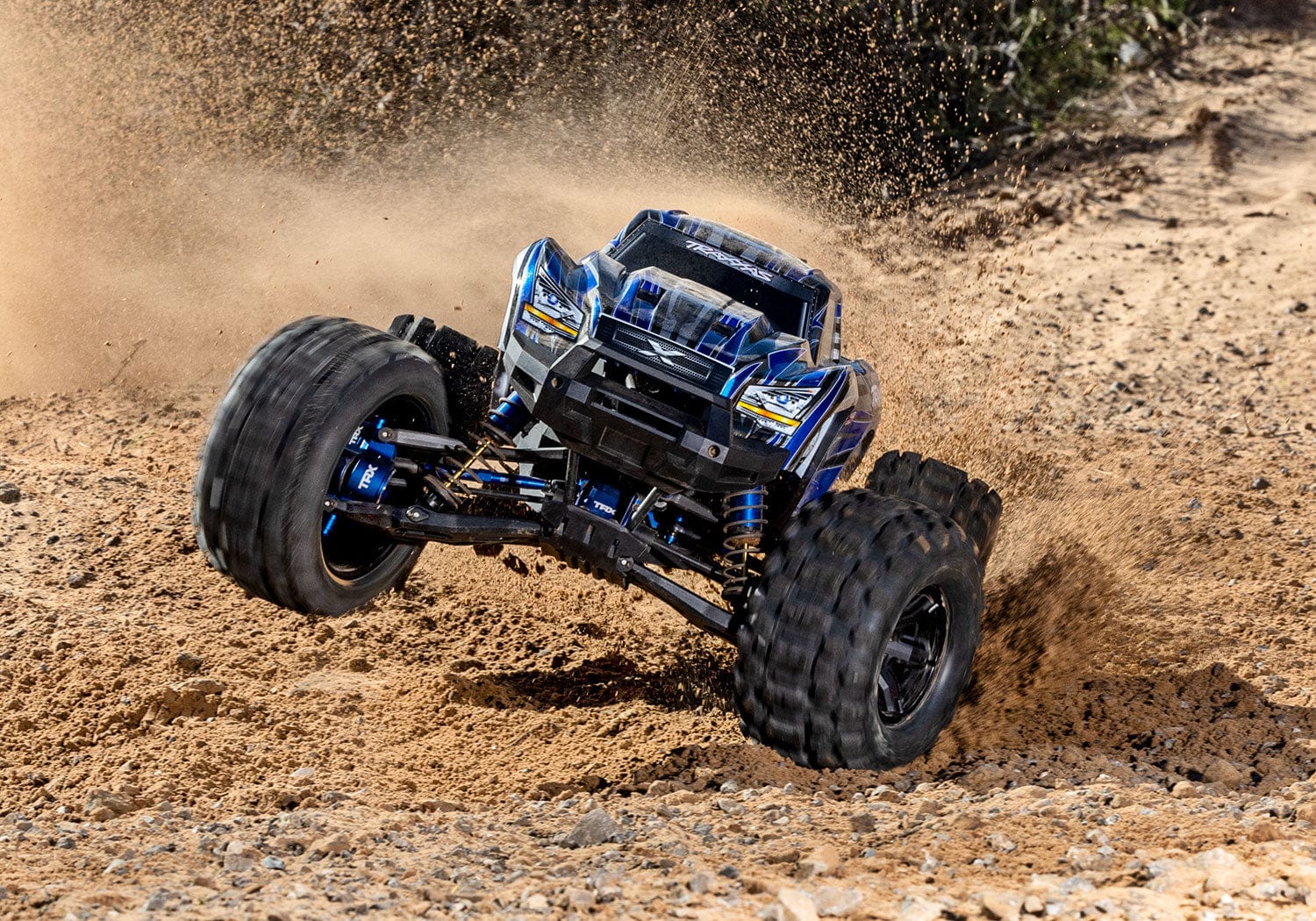 [Action] Traxxas X-Maxx - mavi araç toprak arazide toz bulutu içinde