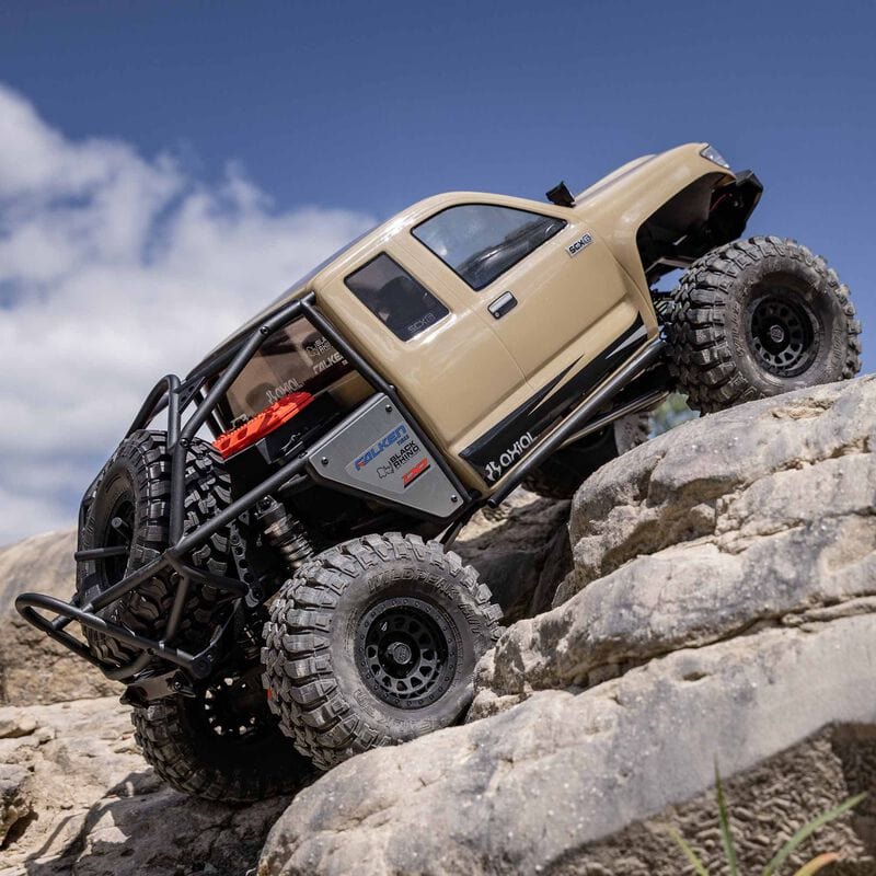 [Action] Axial SCX6 Trail Honcho - kum rengi araç dik kaya tırmanışında, gökyüzü arka planda