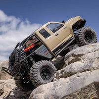 [Action] Axial SCX6 Trail Honcho - kum rengi araç dik kaya tırmanışında, gökyüzü arka planda