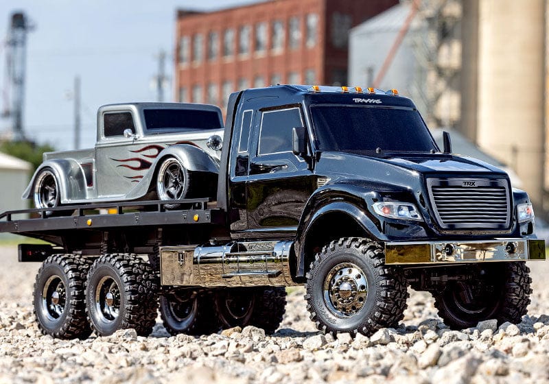 [Action] Traxxas TRX-6 Hauler - çakıl arazide 3/4 önden, gümüş alev desenli hot rod yüklü